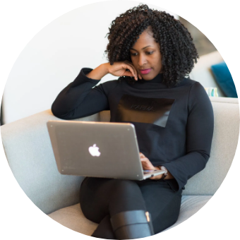 African American Woman Using MacBook on grey couch with white wall in background