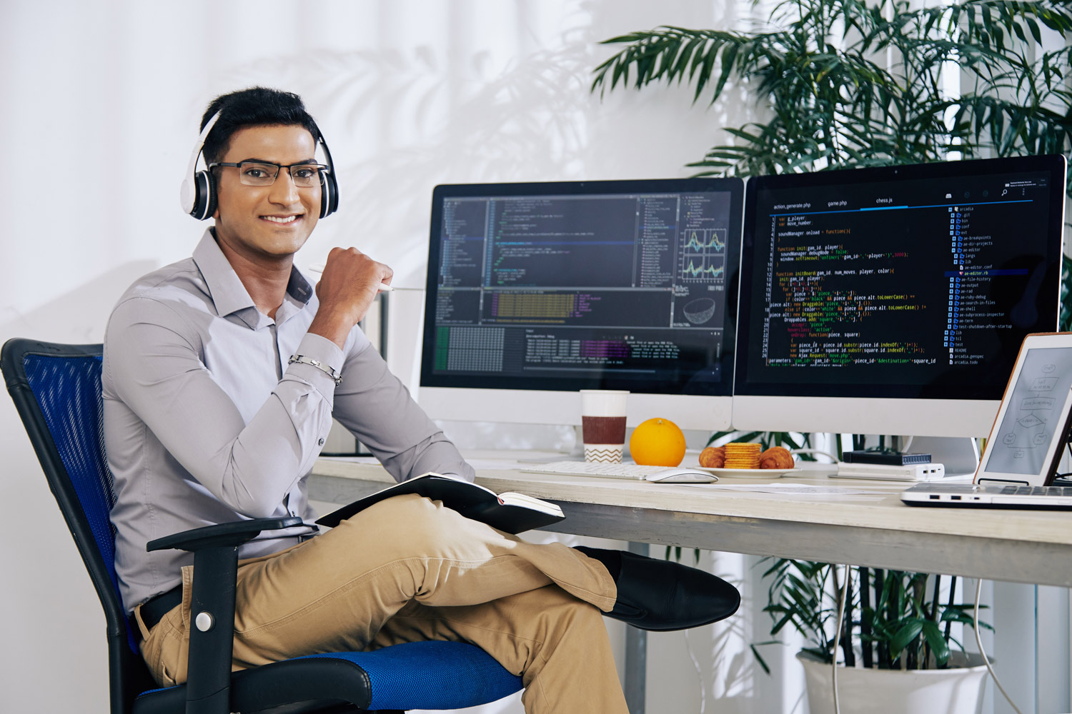 Man sitting at computer with two screens, wearing a headset, looking at camera.
