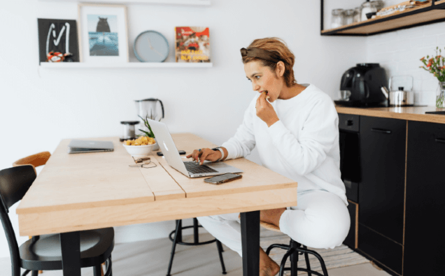 woman coding at kitchen table while having a snack