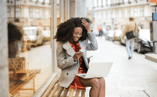 Woman using laptop and phone to apply for Sabio's Women In Tech Scholarship
