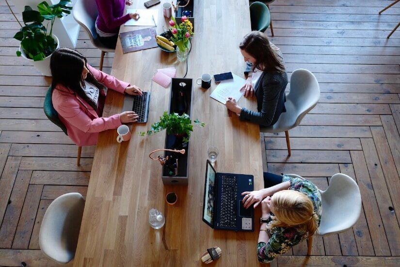 Three women working together in tech around a table.